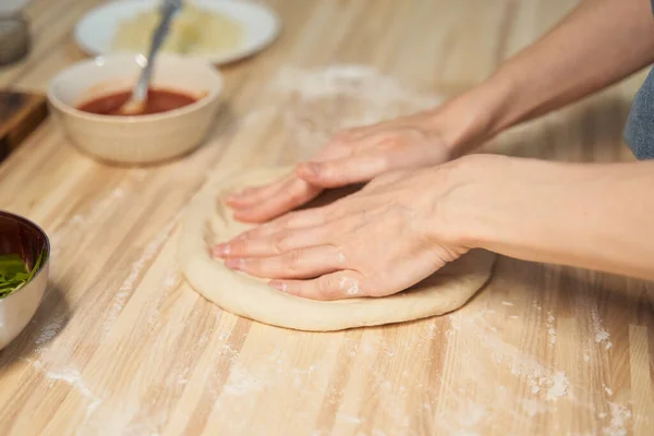 Faceless woman kneading dough on kitchen table at home, apartment. Homemade food
