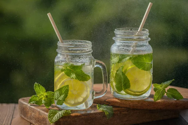 Glasses with lemon water and mint, mojito drink, on a wooden board, outdoors — Stock Photo, Image