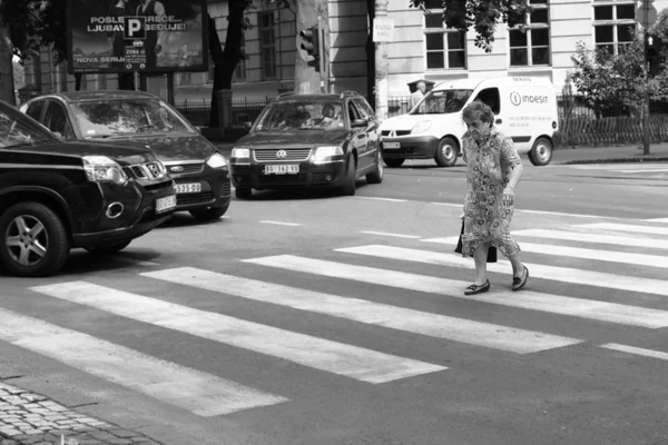 Μια ηλικιωμένη γυναίκα που διασχίζει το δρόμο σε μια διάβαση πεζών με πολλές στάσεις αυτοκίνητα — Φωτογραφία Αρχείου
