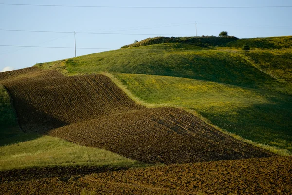 Rolamento paisagístico para a terra arado vermelho e campo verde — Fotografia de Stock