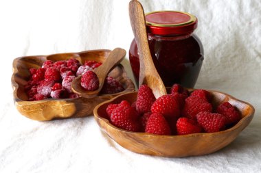 Fresh, frozenraspberry in wooden bowl and raspberry jam in glass jar