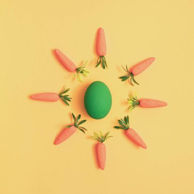 Paskalya yumurtasının etrafındaki havuçlar sarı arka planda yatıyordu.