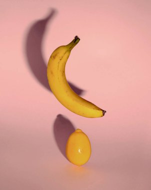 Limonun üzerinde yüzen muz. Pastel puink arka planında soyut minimal kompozisyon