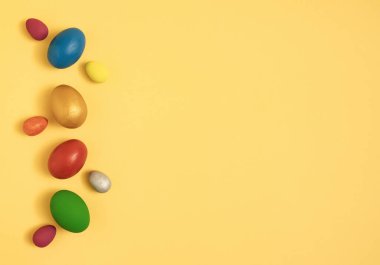 Sarı arka plandaki renkli paskalya yumurtaları kopyalama alanı ile düzleştirilmiş.