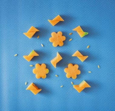 Dilimlenmiş kavun ve kavun çekirdeklerinden yapılmış geometrik şekiller, pastel mavi bir arkaplanda uzanıyordu. Yaz ferahlatıcı konsept, düz konum