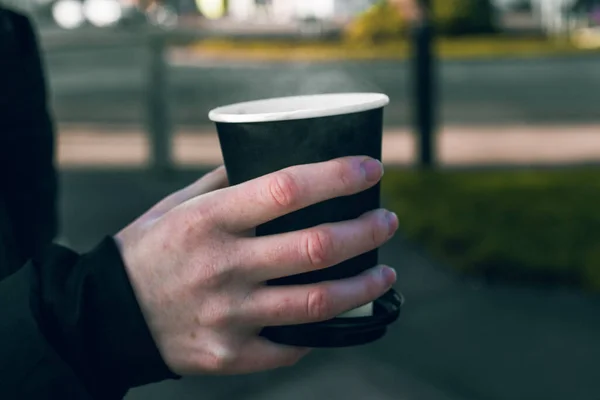 Female person drinking coffee on a cold day in Southsea, Portsmouth. Right hand holding black a take away coffee / tea cup.