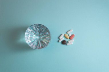 Çok renkli haplar ve mavi arka planda bir bardak su.