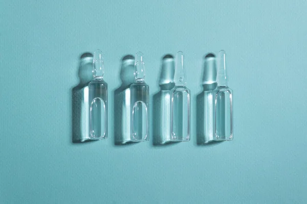 Mavi arka planda koyu gölgeli, sıvı ilaç içeren cam ampuller
