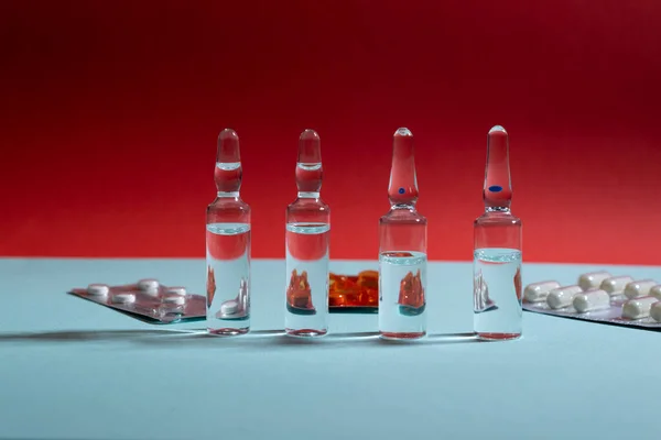 Cam ampuller ve haplar mavi ve kırmızı arka planda su toplamış.