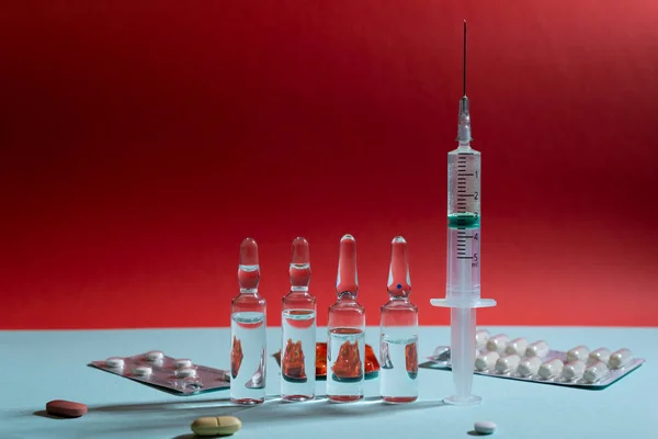 Mavi ve kırmızı zemin üzerinde ilaç bulunan cam ampuller ve şırınga