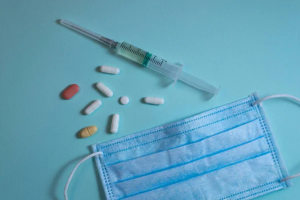 Mavi arka planda duran haplar, şırınga ve yüz maskesi.