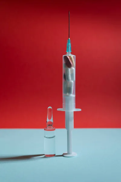 Mavi ve kırmızı arka planda haplarla dolu sıvı ilaç ve şırınga ile cam ampul