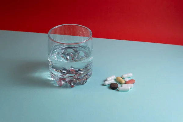 Mavi ve kırmızı arka planda çok renkli haplar ve bir bardak su.