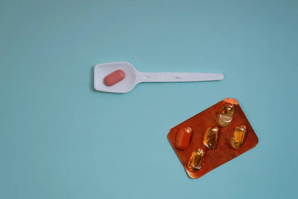 Plastik kaşıkta pembe ve beyaz haplar ve mavi arka planda su toplayan torbalarda haplar.