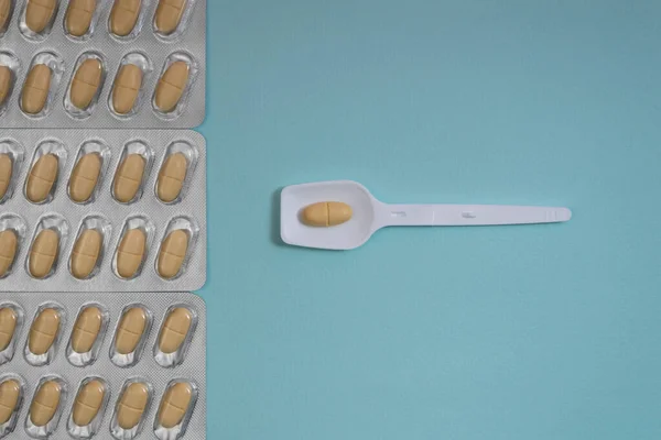 Plastik kaşıkta sarı hap ve mavi arka planda su toplayan haplar.