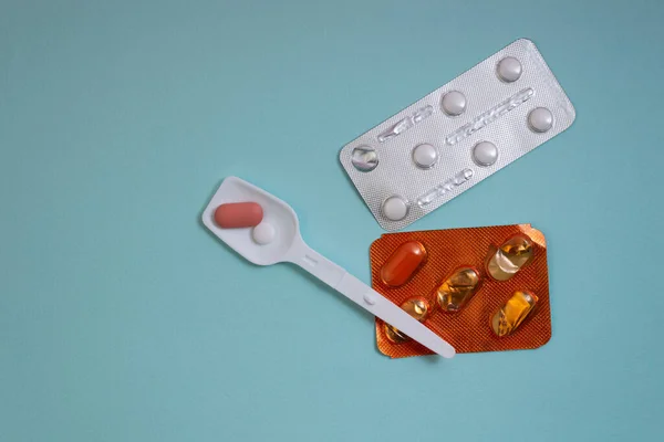 Plastik kaşıkta pembe ve beyaz haplar mavi arka planda su toplayan haplar.