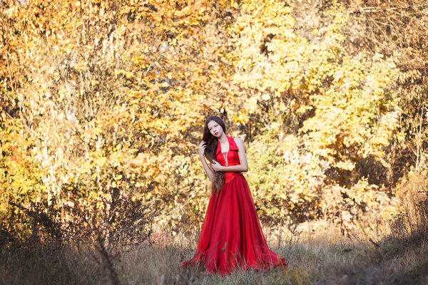 Young girl in red long dress in autumn forest