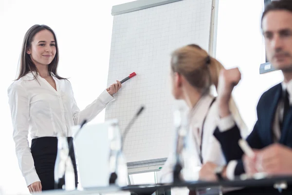 Business woman speaking at presentation and pointing to white board — Stock Photo, Image