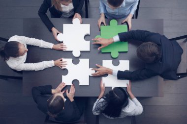 Bir grup iş adamı ofis masasında yapboz yapıyor, üst görünüm, takım desteği ve yardım konsepti, yeşil ve beyaz parçalar