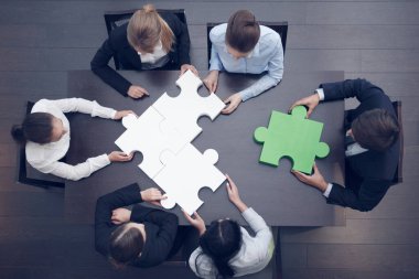 Bir grup iş adamı ofis masasında yapboz yapıyor, üst görünüm, takım desteği ve yardım konsepti, yeşil ve beyaz parçalar