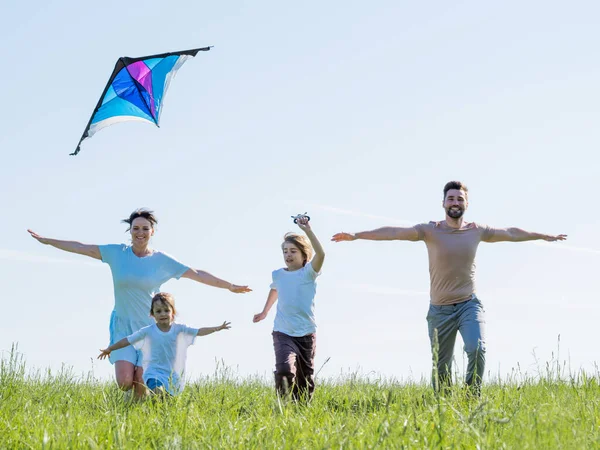 快乐的年轻父母和穿着休闲装的孩子们 一边张开双臂 一边在绿茵的草地上放风筝 一边玩耍 — 图库照片