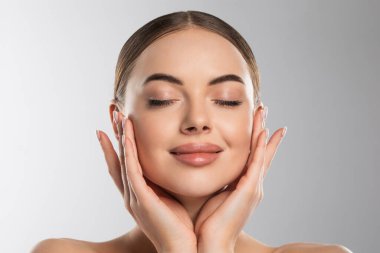 Gri arka planda gözleri kapalı yanaklarını tutarken oldukça mükemmel bir beyaz ten modeli.