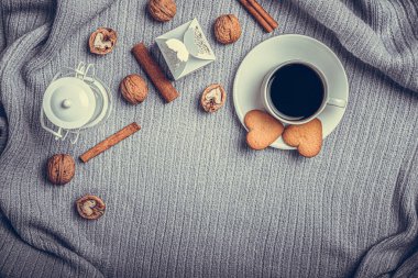 A beautiful plaid, a cup with coffee and cookies on a table with candles and a white envelope.