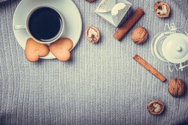 A beautiful plaid, a cup with coffee and cookies on a table with candles and a white envelope.