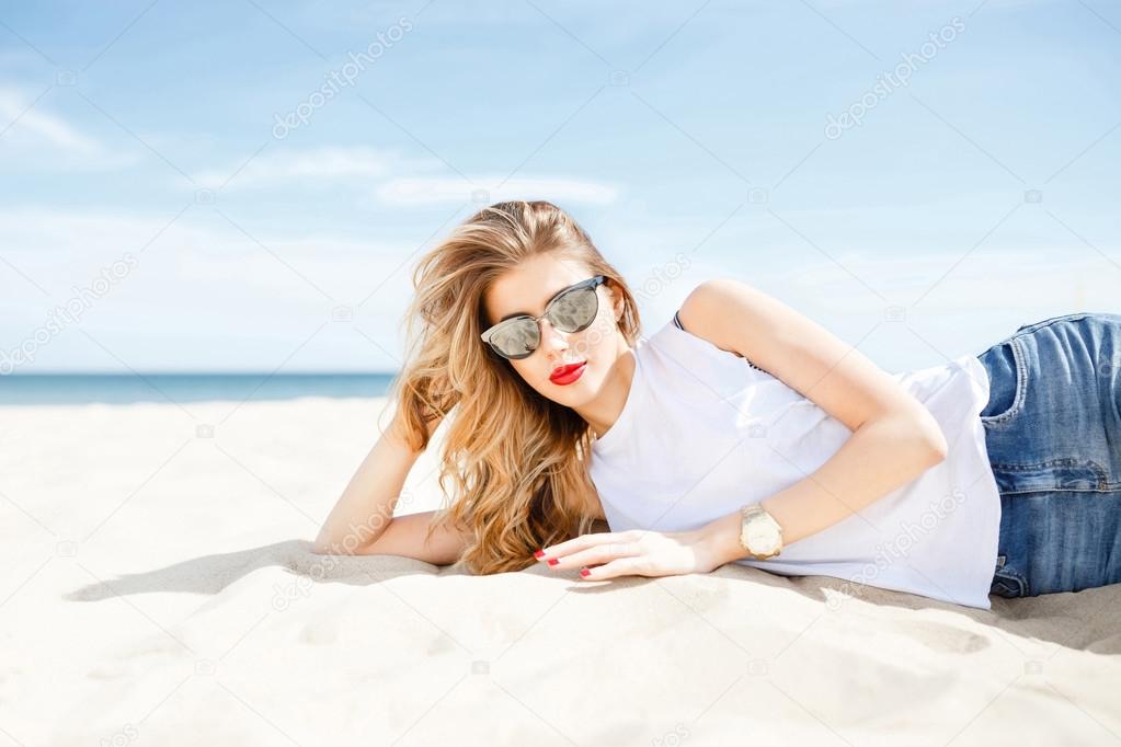 Attractive girl in sunglasses posing lying on the sea beach on a