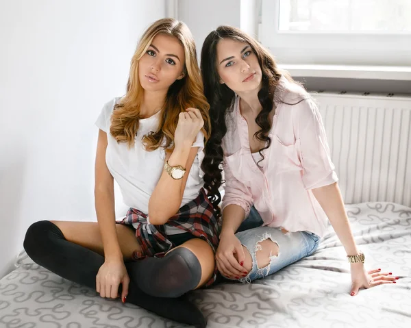 Dos chicas hermosas jóvenes riendo y posando en el dormitorio sentarse — Foto de Stock