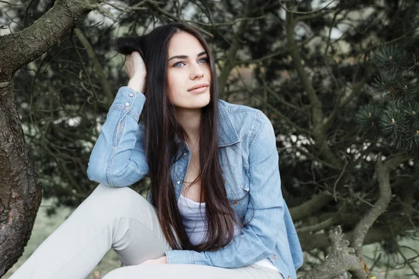 Pretty girl posing in the park on the background of fir trees — Stock Photo, Image