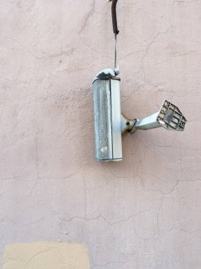 Güvenlik kamerası çıktı ve kabloya takıldı. Holiganlar kırıldı ve çekim işe yaramıyor. Gri ve kahverengi bir duvarın arkasında. Eski ve kirli bir alet.