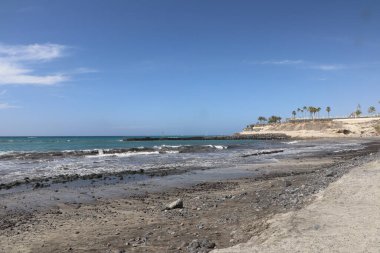 Dalgalar Tener 'de bir kumsalda siyah kum ve kayaların üzerine düşüyor.