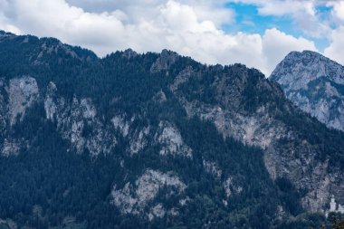 Mavi bulutlu gökyüzünün altındaki yeşil ormanla yüksek Alpler 'in harika manzarası.