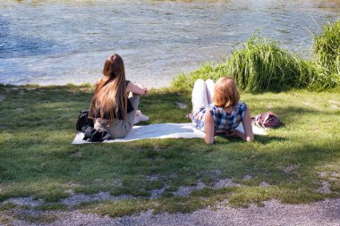 Nehrin kıyısında oturmuş güneşlenen ve konuşan iki genç kadın. Kadın arkadaşlığı.