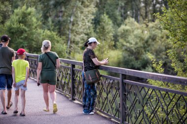 Yazın köprüde parkta yürürken akıllı telefon kullanan bir kadın..