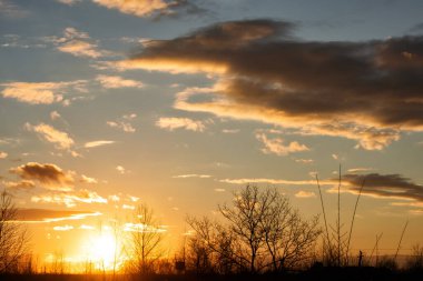 Bulutlu gökyüzünün arkasında parlak bir günbatımı.