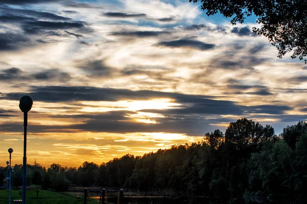 Bulutlu gökyüzünün arkasında parlak bir günbatımı.