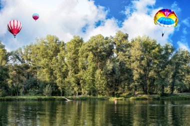 Güneşli bir yaz gününde nehir, orman ve sıcak hava balonları üzerinde paraşütle atlamak..
