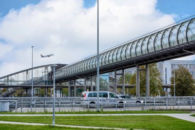 Münih, Almanya - 15 Eylül 2018: Havaalanına giden bir yolun üstündeki cam tünel arka planda bir jet kalkıyor..