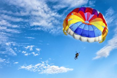 Paragliding using a parachute on background of blue cloudy sky. clipart