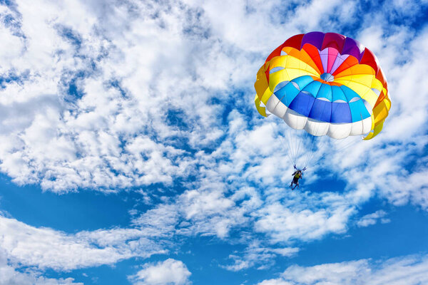 Paragliding using a parachute on background of blue cloudy sky.