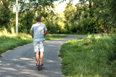 Genç bir adam parkta elektrikli scooter kullanıyor..