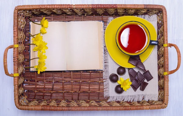 Xícara de chá, chocolate e um livro na bandeja de vime de madeira — Fotografia de Stock