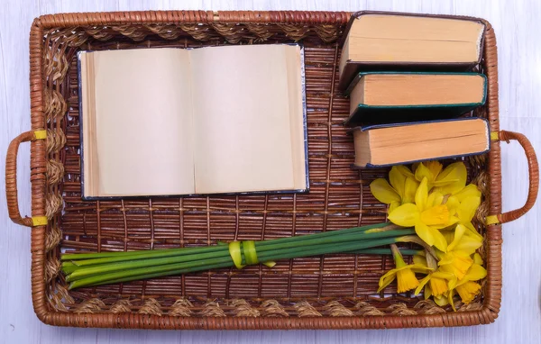 Livro aberto e um buquê de narcisos na bandeja de madeira de vime — Fotografia de Stock