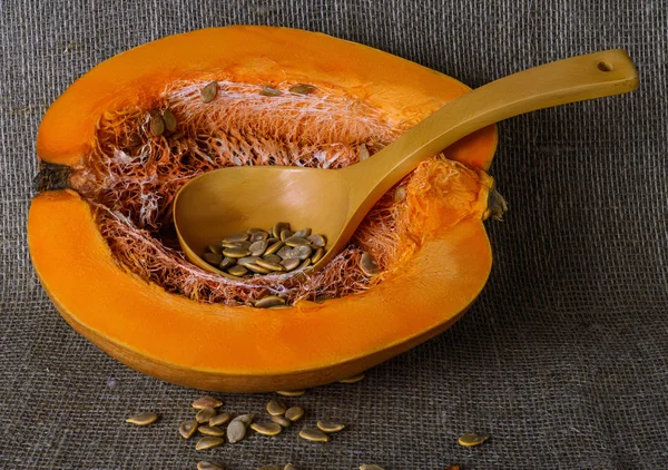 Half a pumpkin and a large wooden spoon with seeds on the background of burlap — Stock Photo, Image