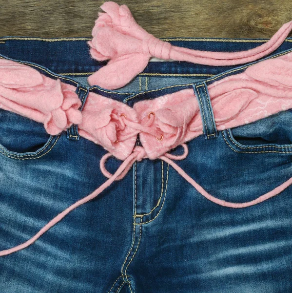 Pink felted  belt with roses in blue jeans on the wooden background