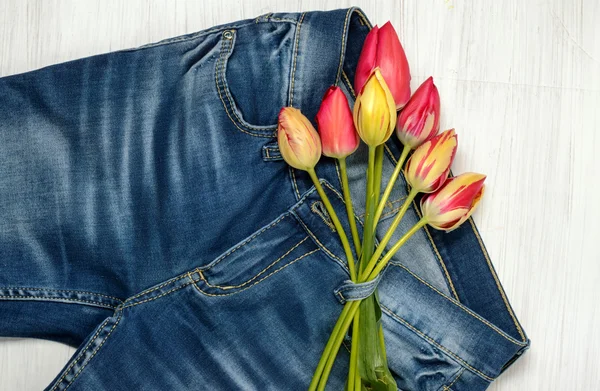 Bouquet of colored tulips and blue jeans on the light background — Stock Photo, Image