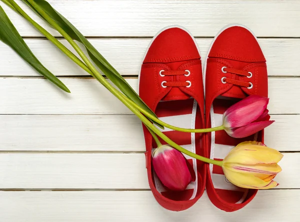 Kırmızı ayakkabılar ve Lale Beyaz ahşap zemin üzerinde bir buket