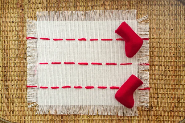 Little red boots on a linen napkin embroidered with red stitches with space for text on the wicker wooden background — Stock Photo, Image